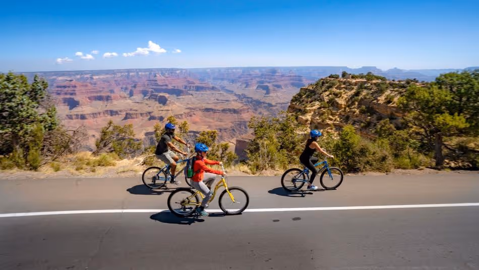 Cyclists riding bikes along scenic road with Grand Canyon vista in background